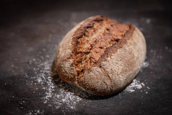 Yakın plan ev yapımı ekşi ekmeğin koyu yüzeye yükselen kabuğu un serpiştirilmiş hali.