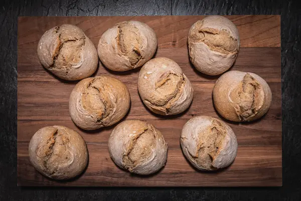 Ev yapımı ekşi hamurdan ruloların kare tahta üzerine dizilmiş, tahta koyu tahta üzerine yerleştirilmiş, neredeyse tüm çerçeveyi dolduran, mükemmel ışıklandırma dokusu