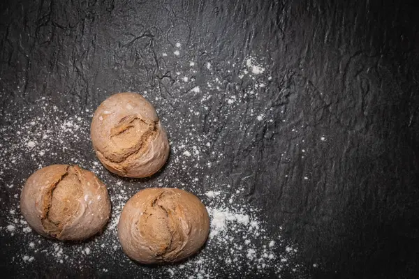 Sol alt köşedeki koyu levha yüzeyine un serpiştirilmiş üç ekşi ekmek, sağ tarafta metin veya tasarım için boş alan