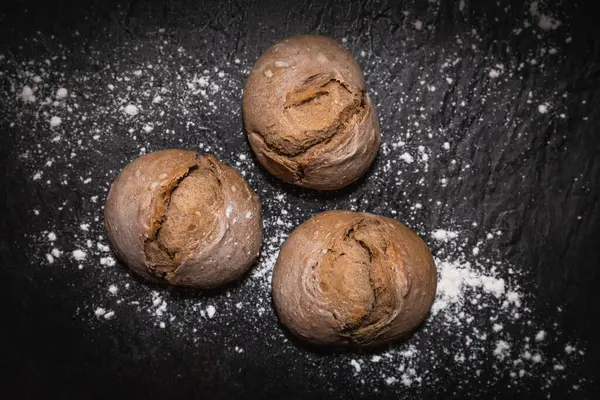 Üç ekşi ekmek rulosunun yakın plan görüntüsü. Koyu levha yüzeyine serpilmiş un serpiştirilmiş. Çerçeveyi dolduruyor.