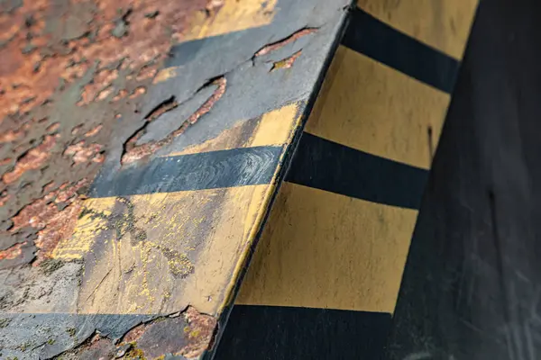 Endüstriyel makinenin köşesindeki siyah ve sarı boyaların yakın plan çekiminde paslı noktalar ve çizikler derinlik ve doku gösteriyor.. 