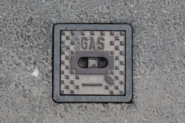 Metal kaplamanın asfalta yakın plan hali. Üstünde GAS kelimesi kabartmalı, yukarıdan simetrik olarak yakalanmış.  