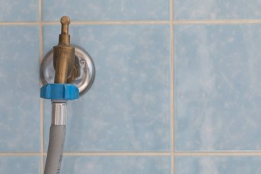 Çamaşır makinesi hortumu bağlantısı olan su musluğunun yakın çekimi, görülebilir hortumun kısa bir kısmı, açık mavi renkli fayanslarla duvara monte edilmiş.