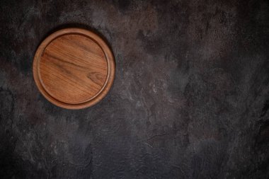 Yuvarlak tahta kesme tahtasının yukarıdan aşağı görüntüsü. Koyu levha yüzeyinde görünür bıçak izleri var. Metin veya tasarım için sağ tarafında boş alan.