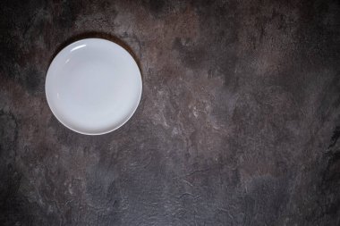 Koyu levha yüzeyindeki beyaz porselen tablonun yukarıdan aşağı görüntüsü, çerçevenin sol tarafında görünür bir doku, sağ tarafında metin veya tasarım için boş alan var