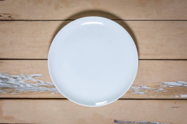 Yukardan aşağı, içi boş beyaz porselen plaka. Eski ahşap masa ve soyulmuş boya.