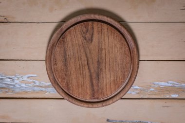 Yuvarlak tahta kesme tahtasının tepeden aşağı yakın çekimi. Bıçak izleri ortada ve eski ahşap masa üzerinde soyulmuş boyayla yakınlaştırılmış.