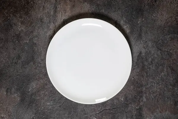 Boş beyaz porselen levhanın tepeden tırnağa yakın planda koyu bir zemin üzerine kuruludur.