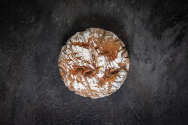 Yuvarlak zanaatkar ekmeği, koyu arkaplan üzerine kuruludur. Yakın planda tepeden tırnağa ışık ve kabuk dokusuyla bile fotoğraflanır.