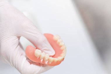 Eldivenli el, temiz tıbbi ortamlarda yıpranmış diş protezi, yakın plan görünüm dişçilikte, protezde veya ağız hijyen işlemlerinde kullanılan üst çene modeli üzerine odaklanmış