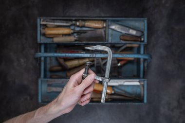 Çeşitli eski aletlerle metal alet kutusunu aç ve karanlık stüdyo ortamında küçük klasik metal kıskaçları tut.  