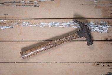 Ahşap saplı eski çekiç, aşınmış bej bir masanın ortasına yerleştirilmiş ve yukarıdan çekilmiş..