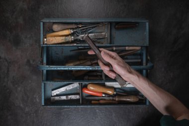 Açık metal alet kutusunun üzerinde el yapımı demir keski var. Karanlık yüzeyde eski aletlerle dolu. Yukarıdan çekilmiş..