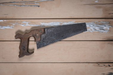 Eski el testeresi yıpranmış bej bir masanın ortasında duruyordu, boyası soyulmuş, yukarıdan çekilmiş..