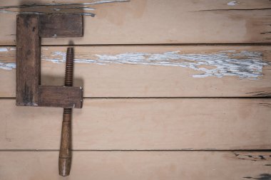 Eski ahşap vida kıskacı, aşınmış bej bir masanın sol tarafında, boyası soyulmuş, yukarıdan çekilmiş. Çerçevenin geri kalanı metin veya tasarım için bir sürü boş alan bırakır.