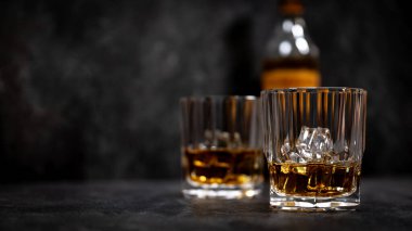 Arka planda buz küpleri olan iki bardak viski. Bardakların arkasına yerleştirilmiş şişe kısmen görünür, bulanık. Resmin sol tarafı metin veya tasarım için boşluk bırakır.