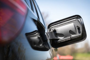 Arabanın arka tarafında açık yakıt kapağını toprak ve aşınmış, ön planda kırmızı stop lambası, arka planda gökyüzü ve yeşilliğin bulanıklaştığı doğal bir ortam görünüyor..