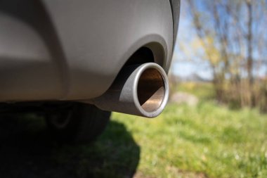 Göz hizasında aşınmış egzoz borusu, çimenlerin doğal arka planı, küçük ağaçlar ve bulanık mavi gökyüzü. Görüntü gerçekçi açık hava kullanımını öneriyor.