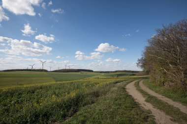 Kırsal alan, toprak yola çıkıyor ve ufuktaki rüzgar türbinleri mavi gökyüzünün altında dağınık bulutlarla birlikte.