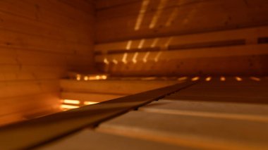 Ön planda ahşap sauna tezgahı net bir odak noktası ve bulanık, sıcak arkaplan yumuşak atmosfer yaratıyor. Yatay 16: 9 biçimi başlık ya da arkaplan için ideal metin alanı.