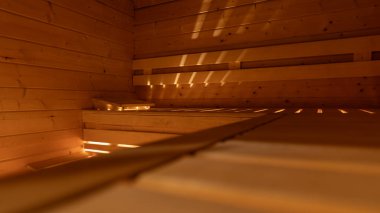 Geniş açılı boş sauna manzarası, sıcak ışıklandırma, ahşap banklar ve arka sıraları gösteriyor. Yatay 16: 9 biçimi, ferah ve temiz sağlık ortamını vurgular.