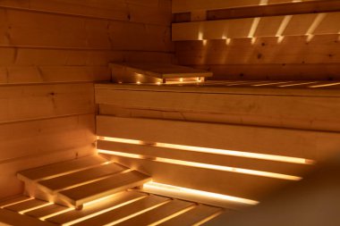 Bankların altından parlayan ışıkla aydınlatılan üst ve alt sıralarda sıcak ahşap başlıklarla dolu boş bir sauna. Huzurlu ve temiz bir atmosfer yaratıyor..  