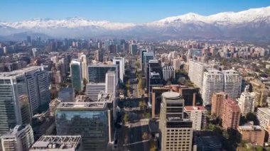Santiago, Şili 23 Mayıs 2024: Drone hiperlapse Las Condes 'teki Apoquindo Bulvarı boyunca ilerlerken arka planda modern binalar, ağaçlarla kaplı caddeler ve karlı And Dağları görünüyor..