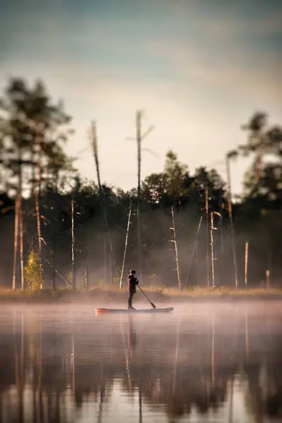 Gün doğumunda sisle çevrili sakin bir gölde sörf yapan bir insan doğanın sükunetini ve dışarıdaki eğlenceyi yakalıyor..