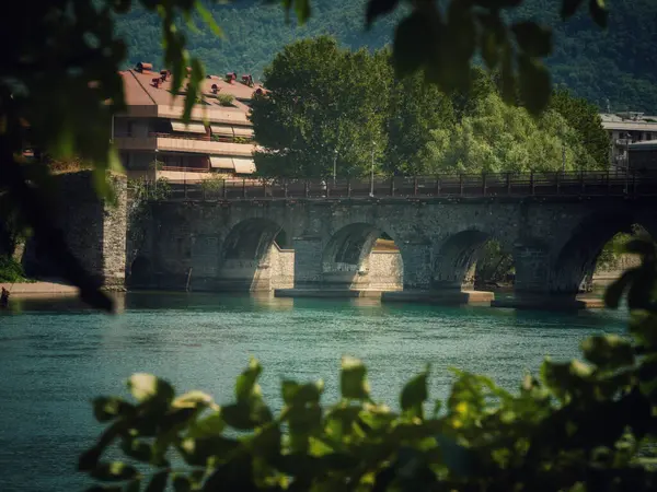 Nehir boyunca uzanan tarihi bir taş köprü, yeşilliklerle çevrili.