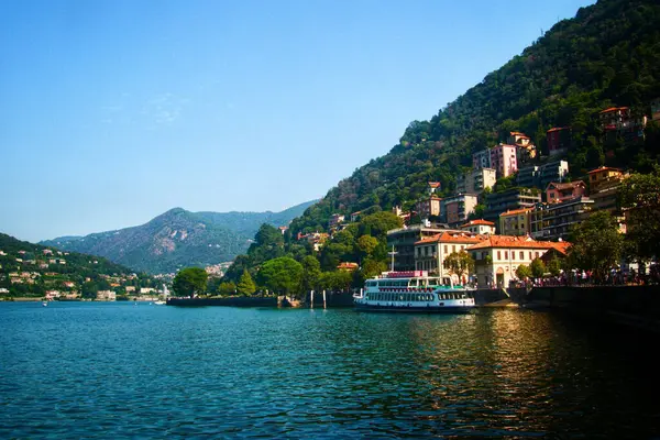 Lecco Gölü manzaralı, yamaçta pitoresk evler ve sahil kenarında turistik bir tekne, turizm ve eğlence için mükemmel bir reklam.