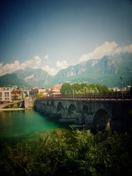 Nehir boyunca uzanan tarihi bir taş köprü, yeşilliklerle çevrili.