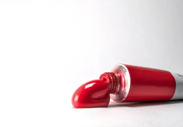 Temiz beyaz bir yüzeye sıkıştırılmış kırmızı renkli az miktarda kırmızı boya içeren bir tüp yakın plan. Sanat, resim, yaratıcılık ve sanatsal malzemelerle ilgili konular için mükemmel.