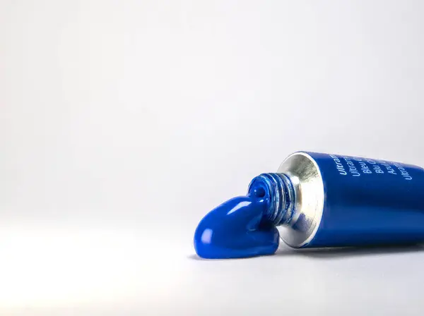 Temiz beyaz bir yüzeye sıkıştırılmış az miktarda canlı mavi boya ile bir tüp ultradeniz mavisi boya yakın çekim