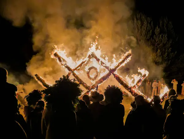 Geleneksel Letonya kostümleri ve çelenkleri içindeki insanlar yaz dönümü kutlamalarında Letonya geleneksel ağaç süsü şeklinde yanan yapıyı izliyorlar.