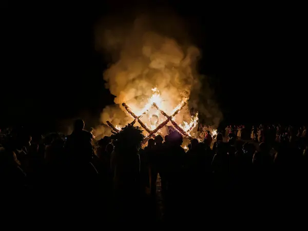 Geleneksel Letonya kostümleri ve çelenkleri içindeki insanlar yaz dönümü kutlamalarında Letonya geleneksel ağaç süsü şeklinde yanan yapıyı izliyorlar.