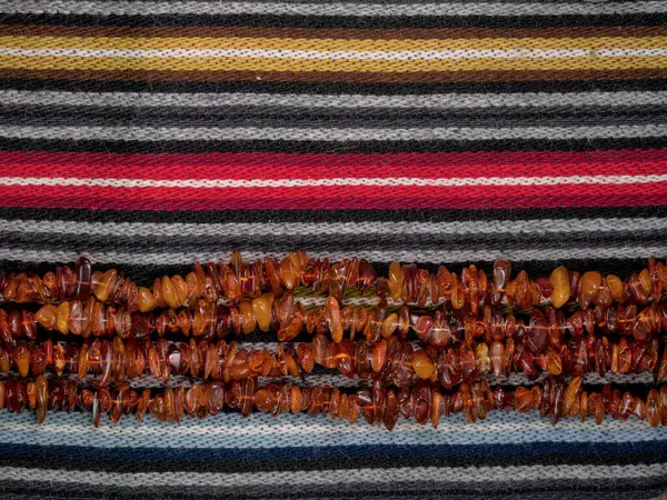 Kehribar boncukları renkli yün kumaşlarda yatay olarak dizilmiş.