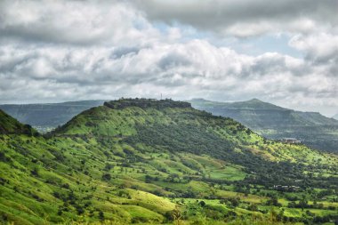Satara, Maharashtra 'daki yeşil tepelerin ve vadilerin manzarası, canlı bitki örtüsü ve bulutlu gökyüzü sakin bir atmosfer yaratıyor..