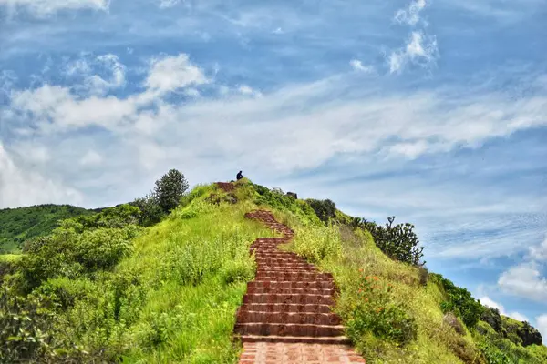 Dolambaçlı bir tuğla yolu Satara, Maharashtra 'nın batısındaki yemyeşil manzaralar boyunca uzanır, dağınık mavi bulutlarla dolu canlı bir gökyüzünün altında..