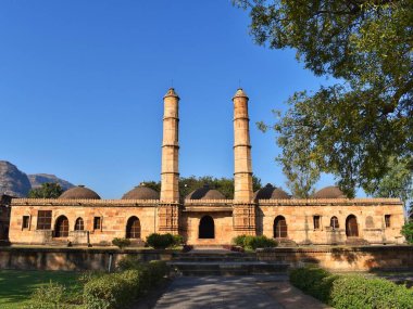 Gujarat 'taki Champaner-Pavagad Arkeoloji Parkı' ndaki tarihi Saher-ki-Mescid, açık mavi gökyüzü ve yemyeşil bir gökyüzüne karşı güneş ışığında yıkanan, ikiz minareler ve kubbelerle karışık İslami mimariyi gözler önüne seriyor..