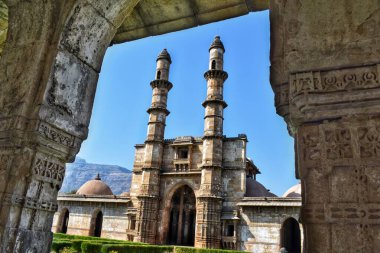 Champaner, Gujarat 'taki görkemli Jami Mescidi girişi, iki minareyi sergiliyor. Detaylı bir taş kemerle çerçevelenmiş, dingin mimari ve mavi gökyüzü ile çevrili..