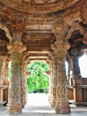 Modhera Güneş Tapınağı Gujarat 'taki Sabha Mandapa' nın doğu girişinde süslü sütunlar oyulmuş, karmaşık taş işçiliği ve doğal yeşillikler arasında antik mimari detaylar sergilenmektedir..