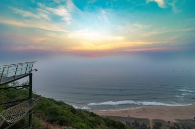 Dolphin Cove 'dan görüldüğü gibi, Visakhapatnam, Yarada Sahili' nin sakin bir gündoğumu manzarası. Yumuşak dalgalar yumuşak, renkli bir gökyüzünün altında kumlu sahille buluşur..