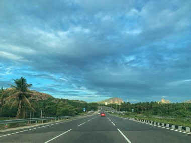 Bangalore ve Mysore arasında, Ramnagara 'nın yeşil ve kayalık tepeleriyle çevrili, parlak, parçalı, mavi gökyüzü altında ulusal bir otoyol..