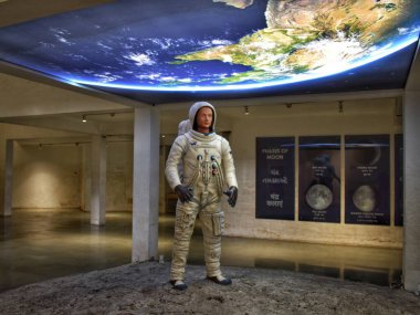 Astronot mankenler Vadodara 'da, Gujarat uzay sergisinde ışıklandırılmış Dünya arkaplanı altında, ay faz posterleri ve parlak iç mekanlar sergileniyor..