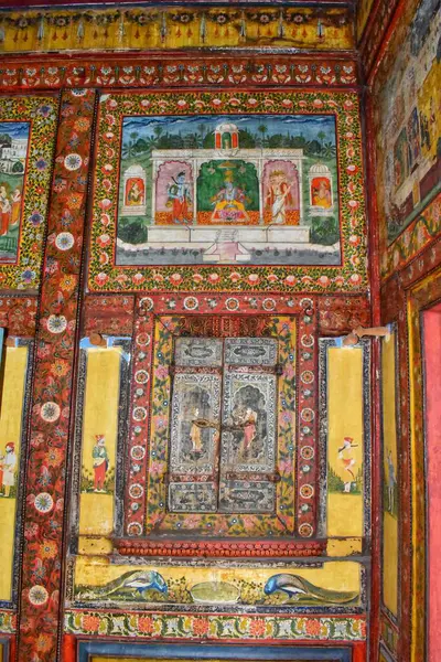 Gujarat, Vadodara 'da tarihi bir bina olan 150 yıllık Tambekar Wada' nın içindeki karmaşık oyulmuş ahşap kapıyı çevreleyen renkli Hindu mitolojik duvar resimleri..