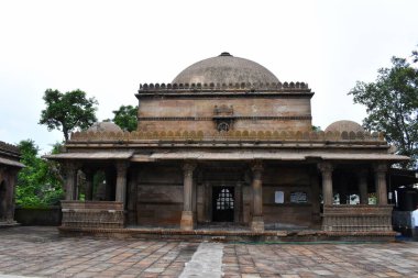 Ahmedabad, Gujarat 'taki Dai Halima Sultani Camii' nin tarihi cephesinde karmaşık taş mimari, kubbeler ve bulutlu bir günde çevresini çevreleyen yeşil bir avlu yer alıyor..