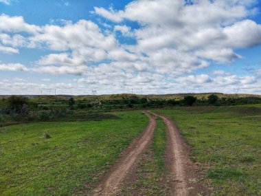 Kiraksal, Satara 'da sakin bir kırsal manzara, dağınık bulutlarla dolu canlı bir gökyüzünün altındaki yemyeşil çayırlarda dolanan kirli bir patikayı gösteriyor..