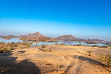 Jawai, Rajasthan 'ın nefes kesici manzarası, sakin Jawai Bandosu, kurak çöl arazisi, ve açık mavi gökyüzünün altındaki engebeli tepeler.