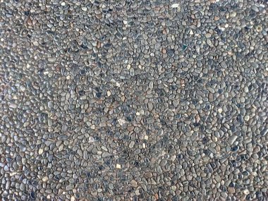 Asfaltlı asfalt yüzeyin detaylı bir yakın çekimi tutarlı dokusunu ve güneş ışığındaki küçük taş kümesini gözler önüne seriyor.