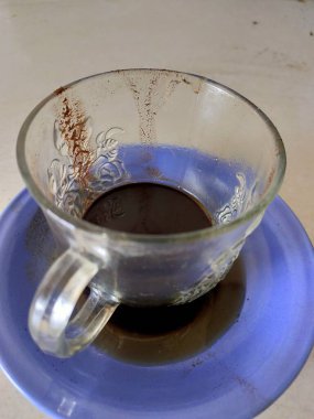 Bitmiş bir sabah ritüelini işaret eden, mavi bir fincan üzerindeki neredeyse boş bir cam kahve fincanı. Kafein molasının rahatlığını ve sonunu yakalar.